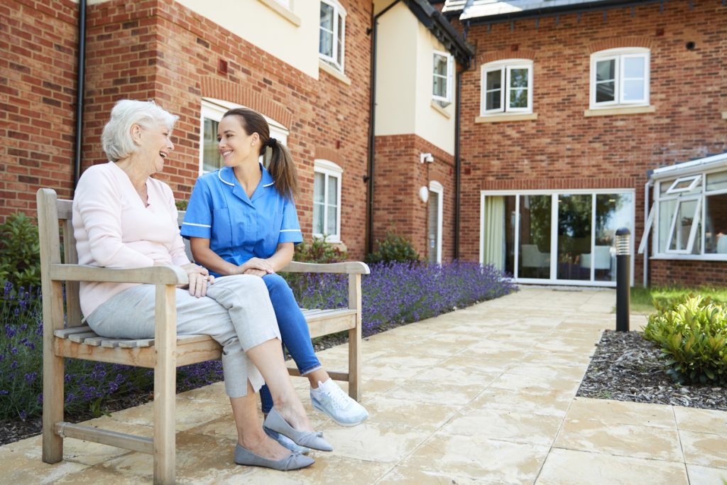 Senior woman sitting on bench with nurse and talking