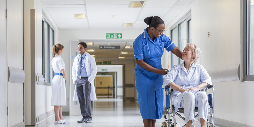 Caregiver assisting a patient in a wheelchair while a doctor stands in the background